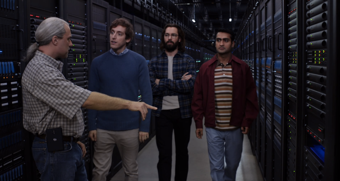 Still from Silicon Valley, a character is pointing at servers in a data centre while the other characters are observing