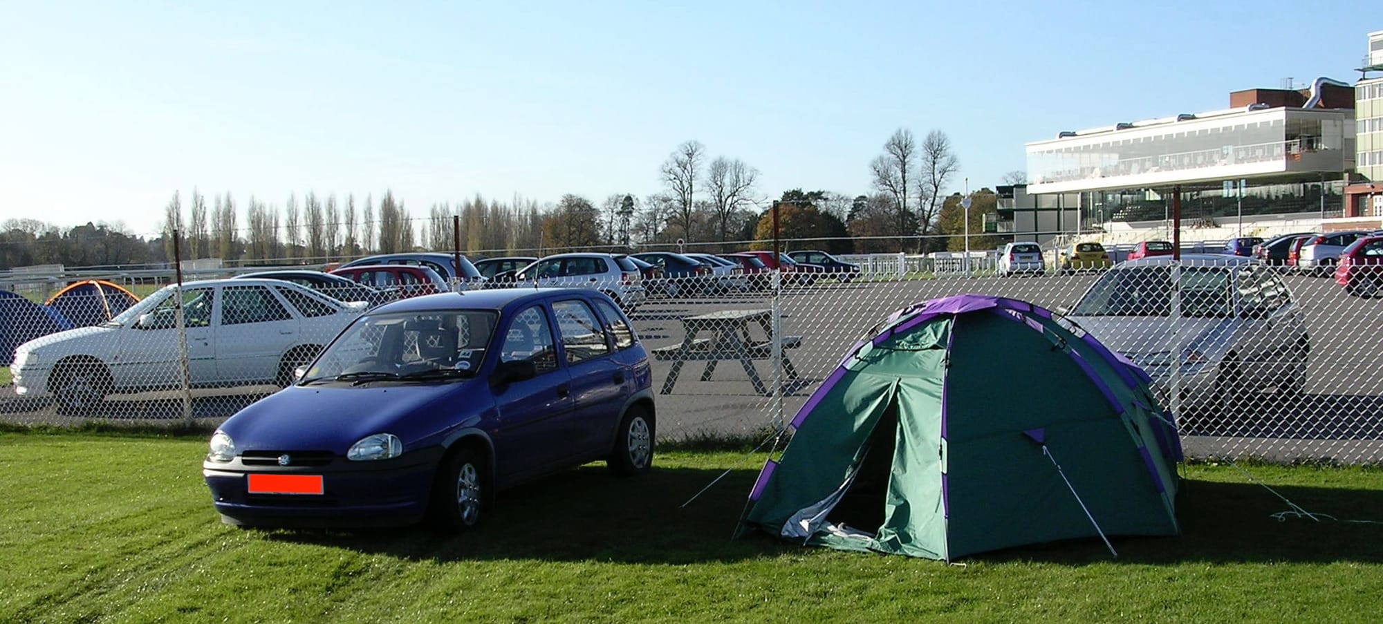 Photo in a car park next to a field - lots of cars parked, with a tent in the foreground