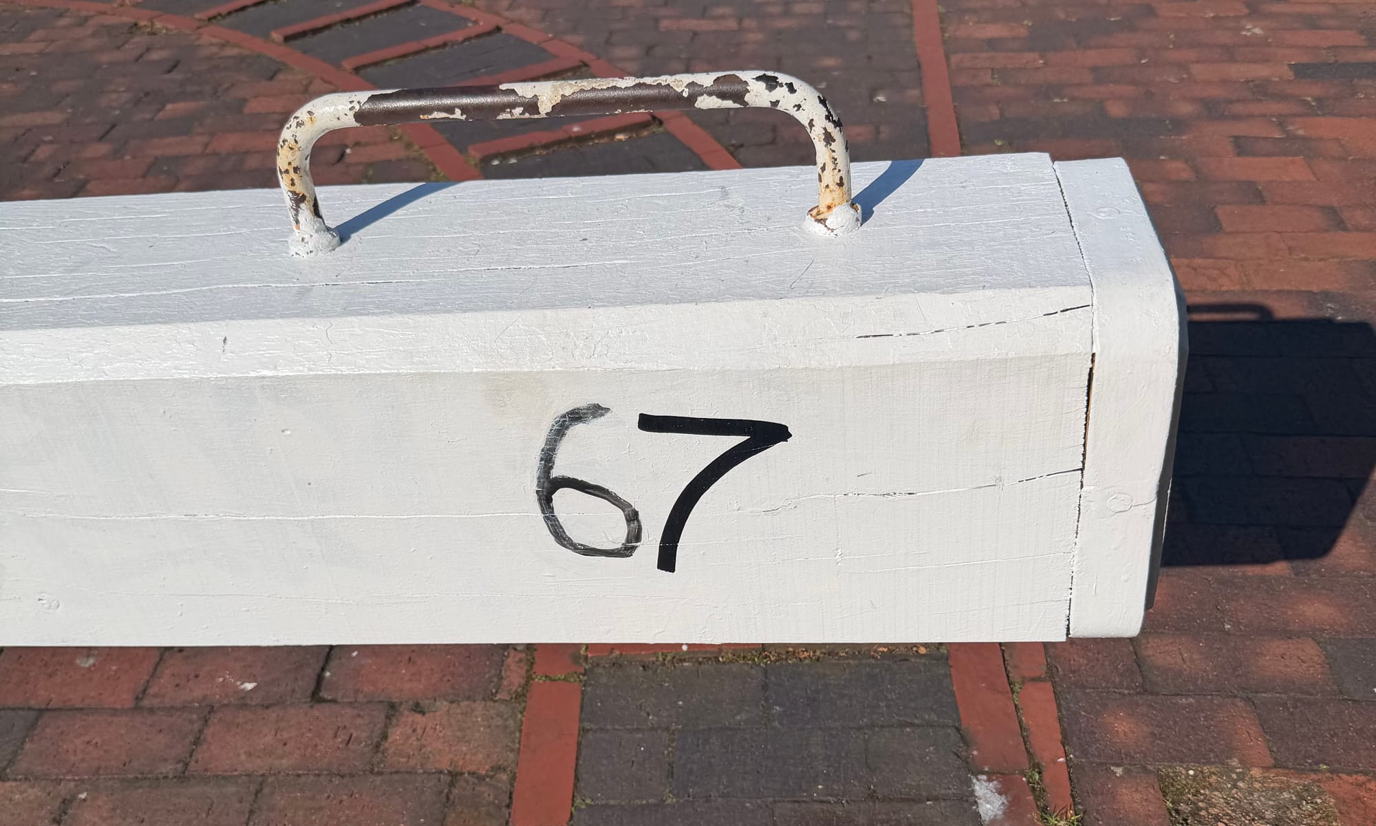 A lock paddle painted white with the lock number 7, with grafitti adding a "6" before it to read 67