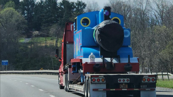 Photo of Thomas the Tank Engine on the back of a truck, with its face blanked out 